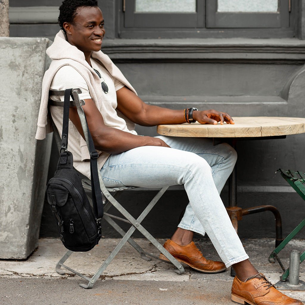 Smiling man seated at a café table with a black leather backpack beside his chair