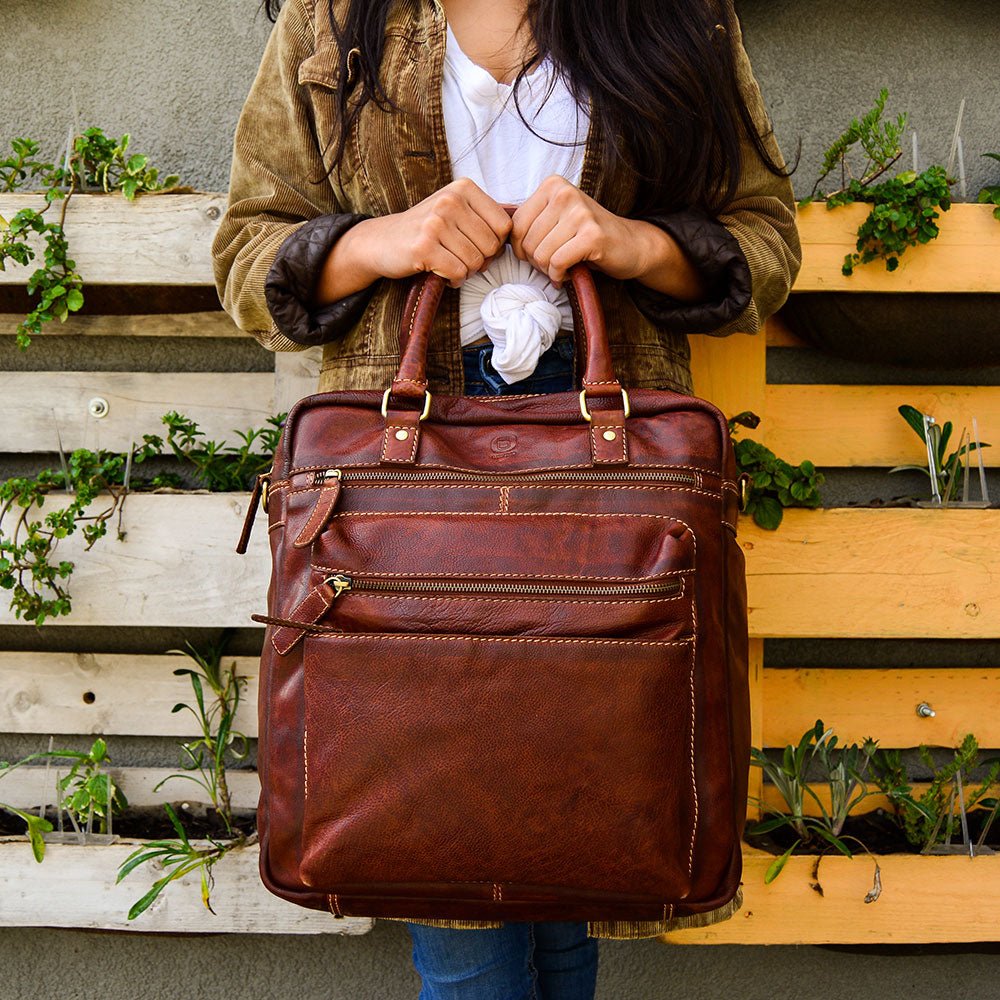 Woman holding a brown leather backpack in front of a wooden planter wall
