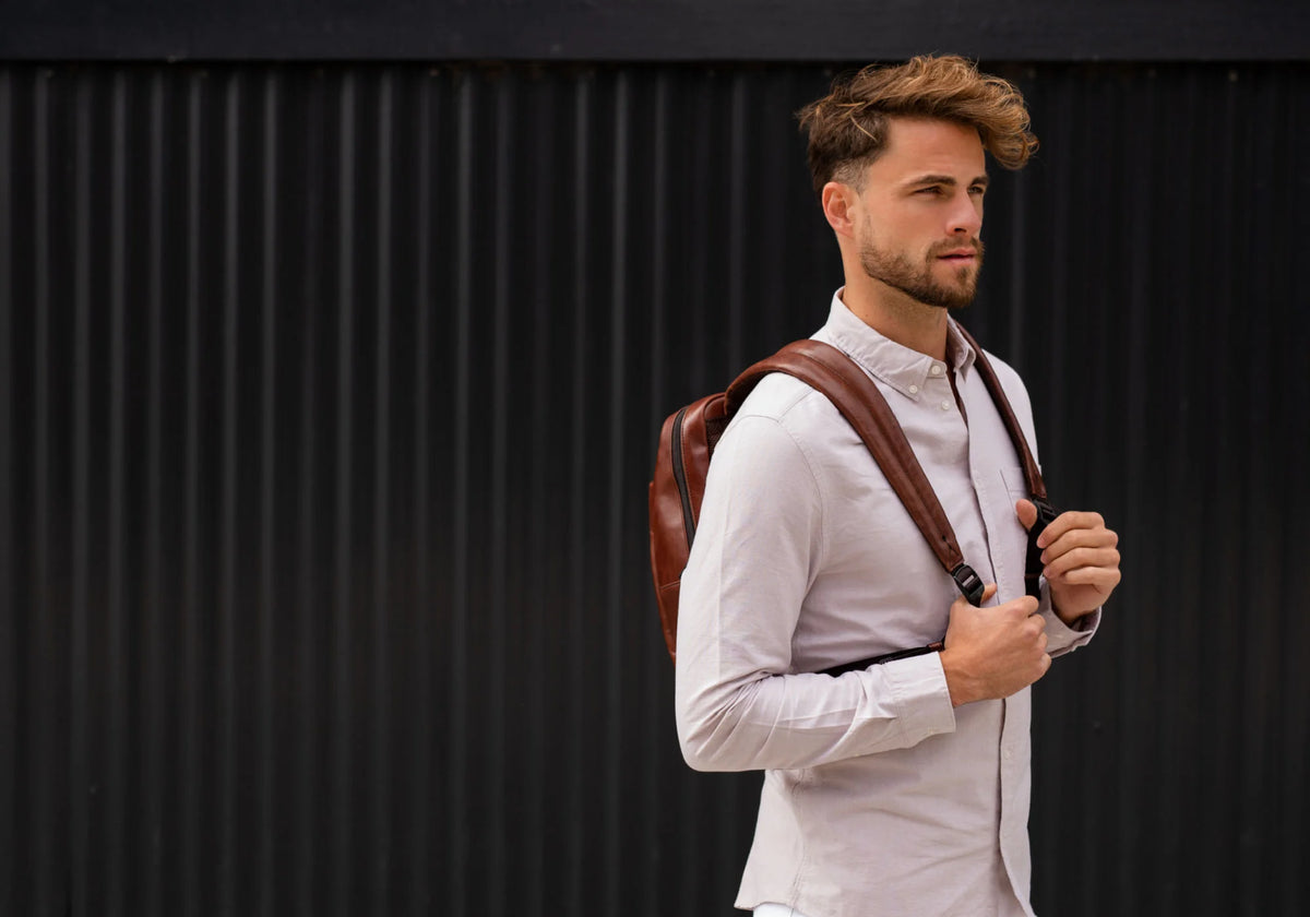 Man in a light shirt holding the straps of a brown leather backpack