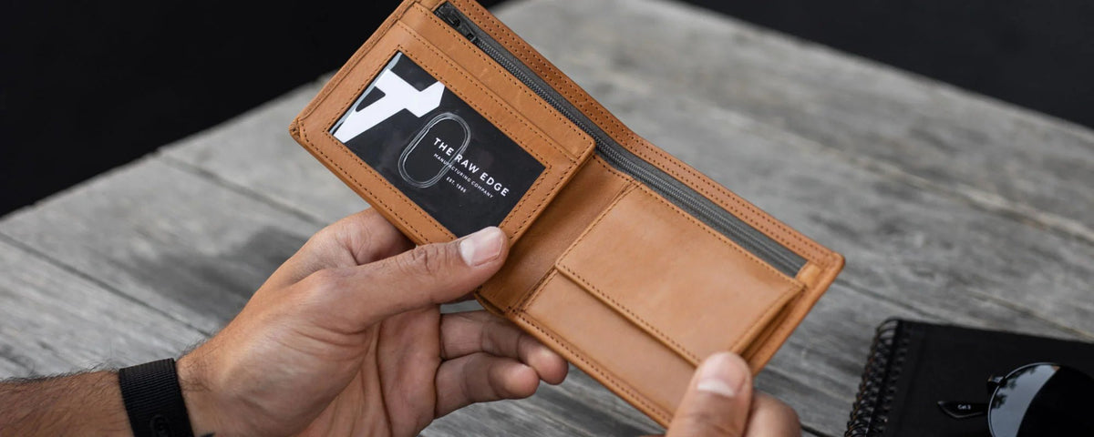 Hands opening a tan leather wallet showing an ID window and coin pocket