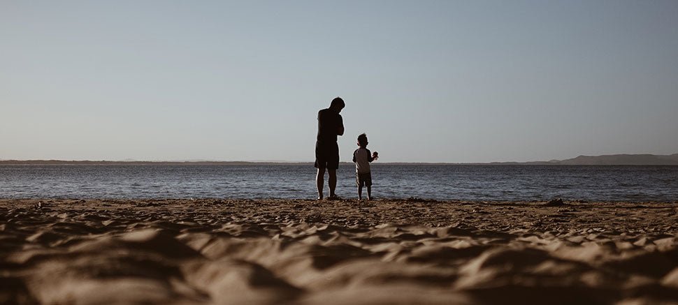 Father and young child silhouetted on a beach at dusk