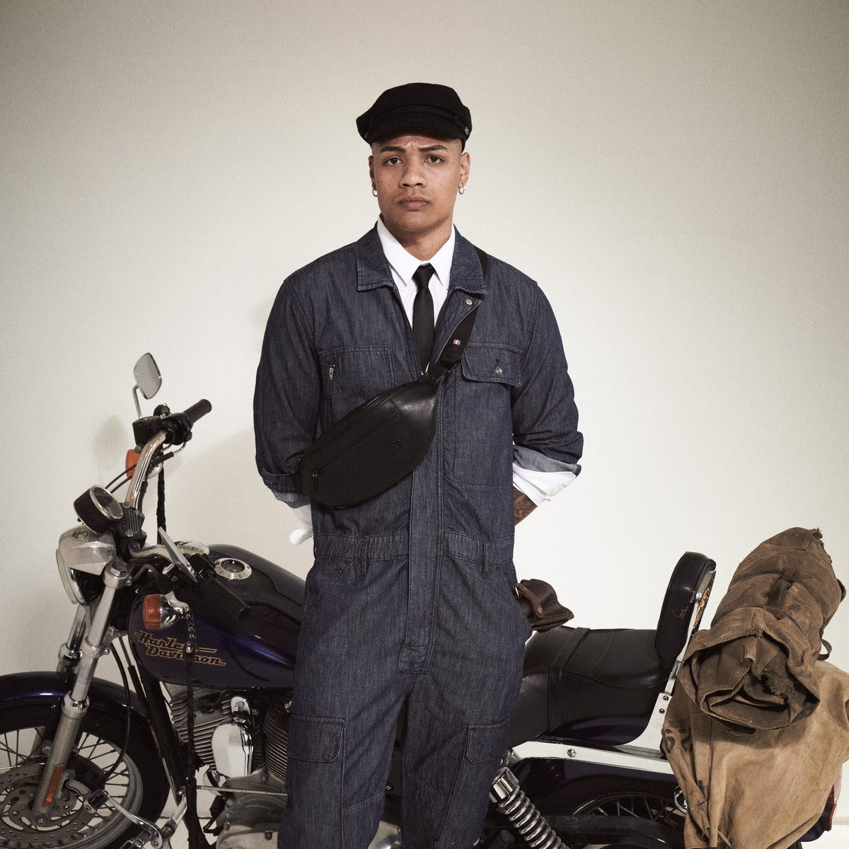 Man in a denim boilersuit and cap wearing the black Bell Waist Bag beside a motorbike