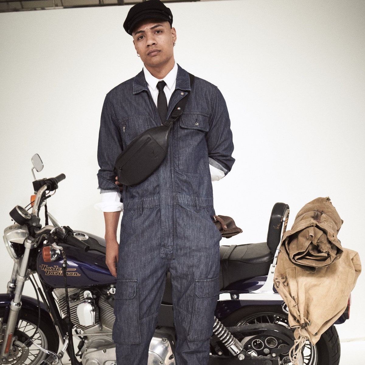 Black Bell Waist Bag worn crossbody, full-length view of a man in denim next to a motorbike