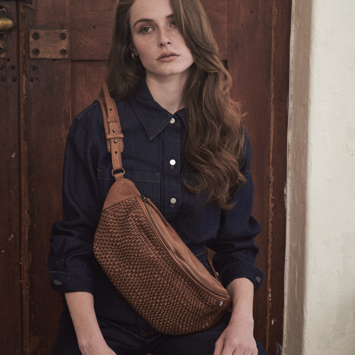 Close view of the Bell Waist Bag in cognac worn high across the chest, woven front and zip