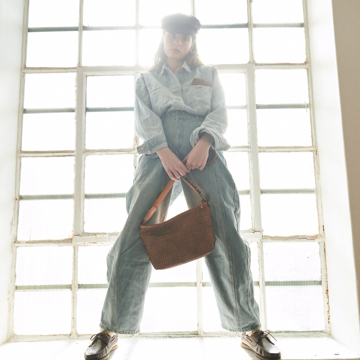 Woman in denim holding the cognac Bell Waist Bag by its strap in front of a tall window