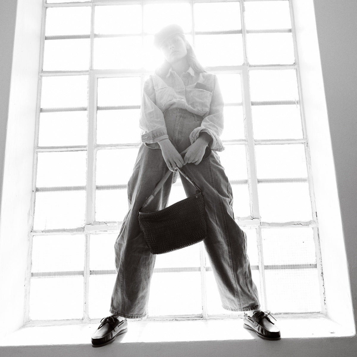Black and white shot of the Bell Waist Bag held by its strap in front of a tall studio window