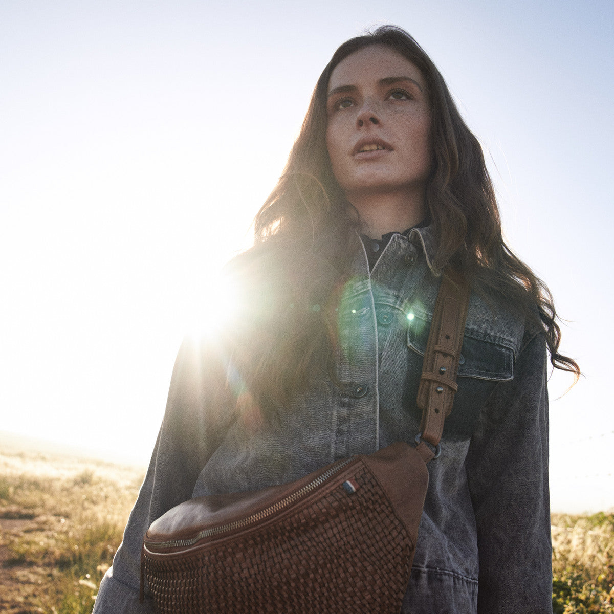 Woman in sunlight wearing the Bell Waist Bag in cognac with its buckled leather strap