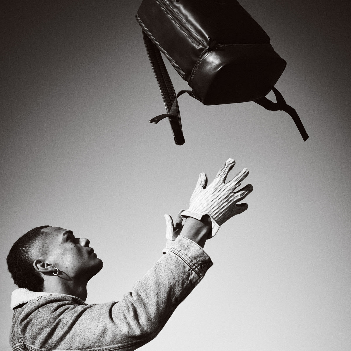 Black and white shot of the James Laptop Backpack thrown in the air towards a man's hands