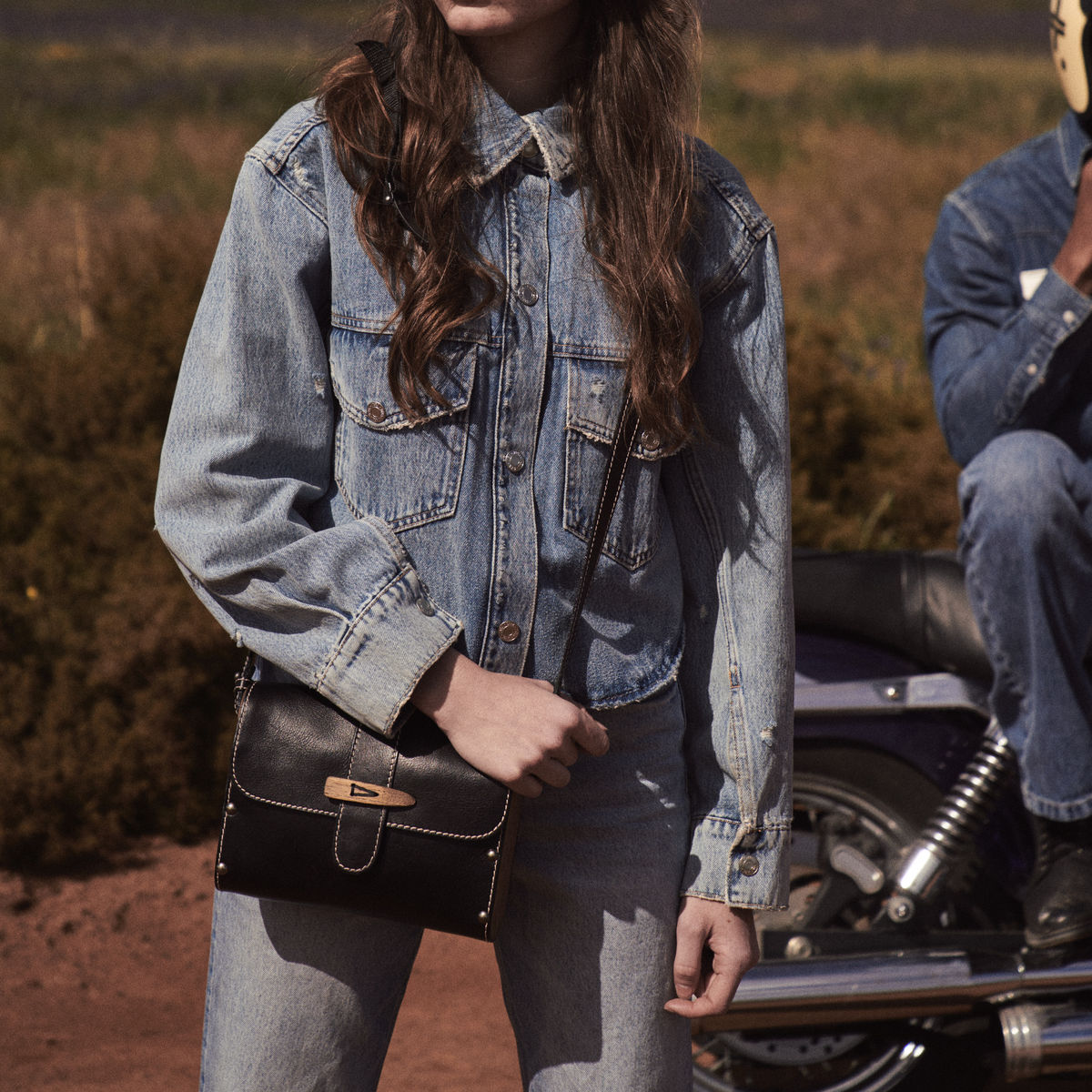 Black Sally satchel with wooden toggle held at the hip over a light denim jacket