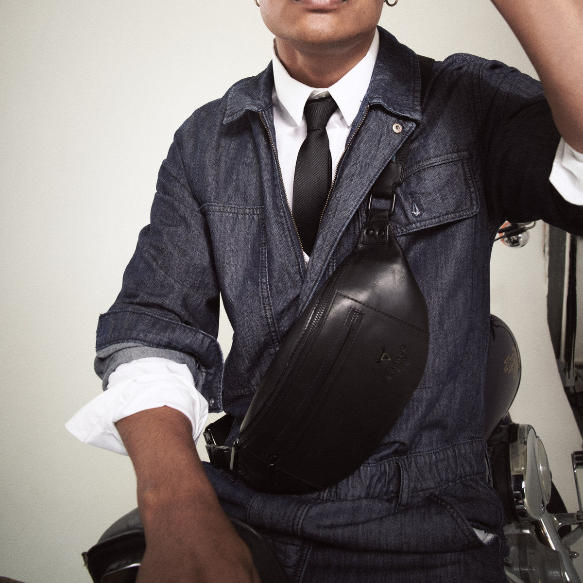 Bell Waist Bag in black worn across the chest of a man in a denim boilersuit and tie