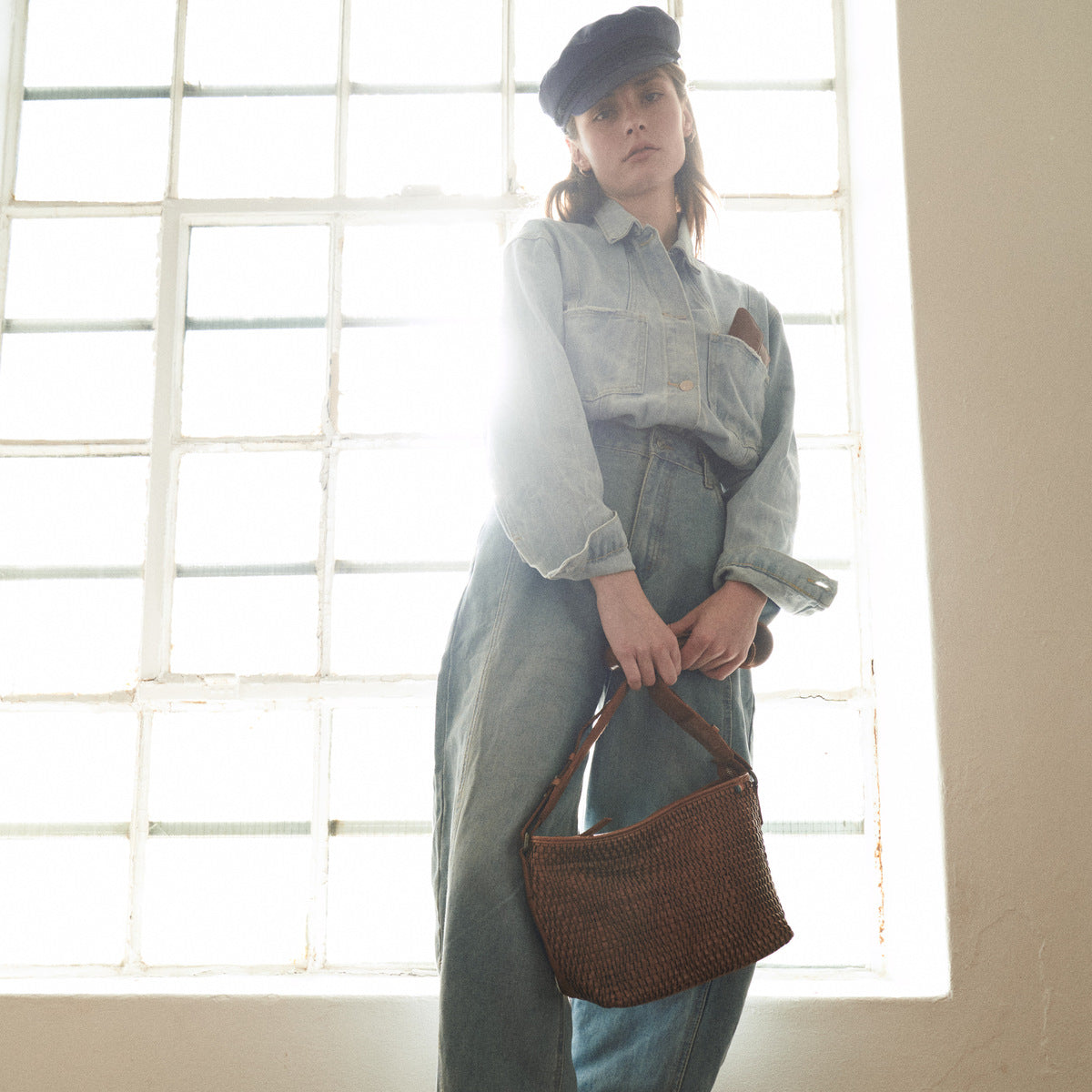 Cognac Bell Waist Bag carried by its strap by a woman in denim standing at a bright window