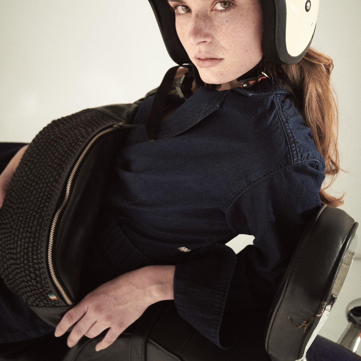 Woman in a cream helmet leaning on the black woven Bell Waist Bag on a motorbike