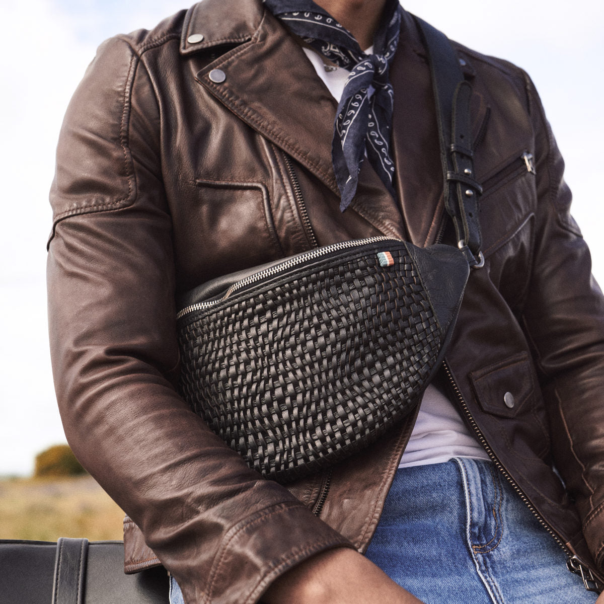 Bell Waist Bag in black woven leather worn across a brown leather biker jacket