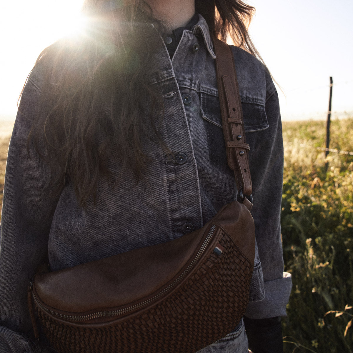 Close-up of the cognac Bell Waist Bag woven front and smooth leather top in backlit sun