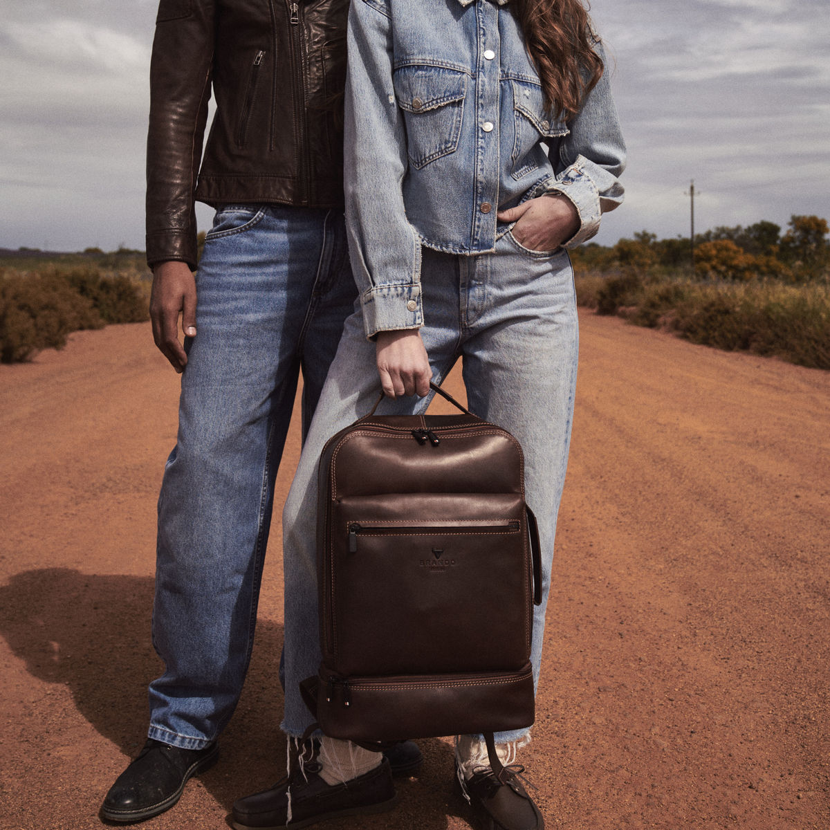 Brown James Laptop Backpack held by its top handle by a woman on a red dirt road