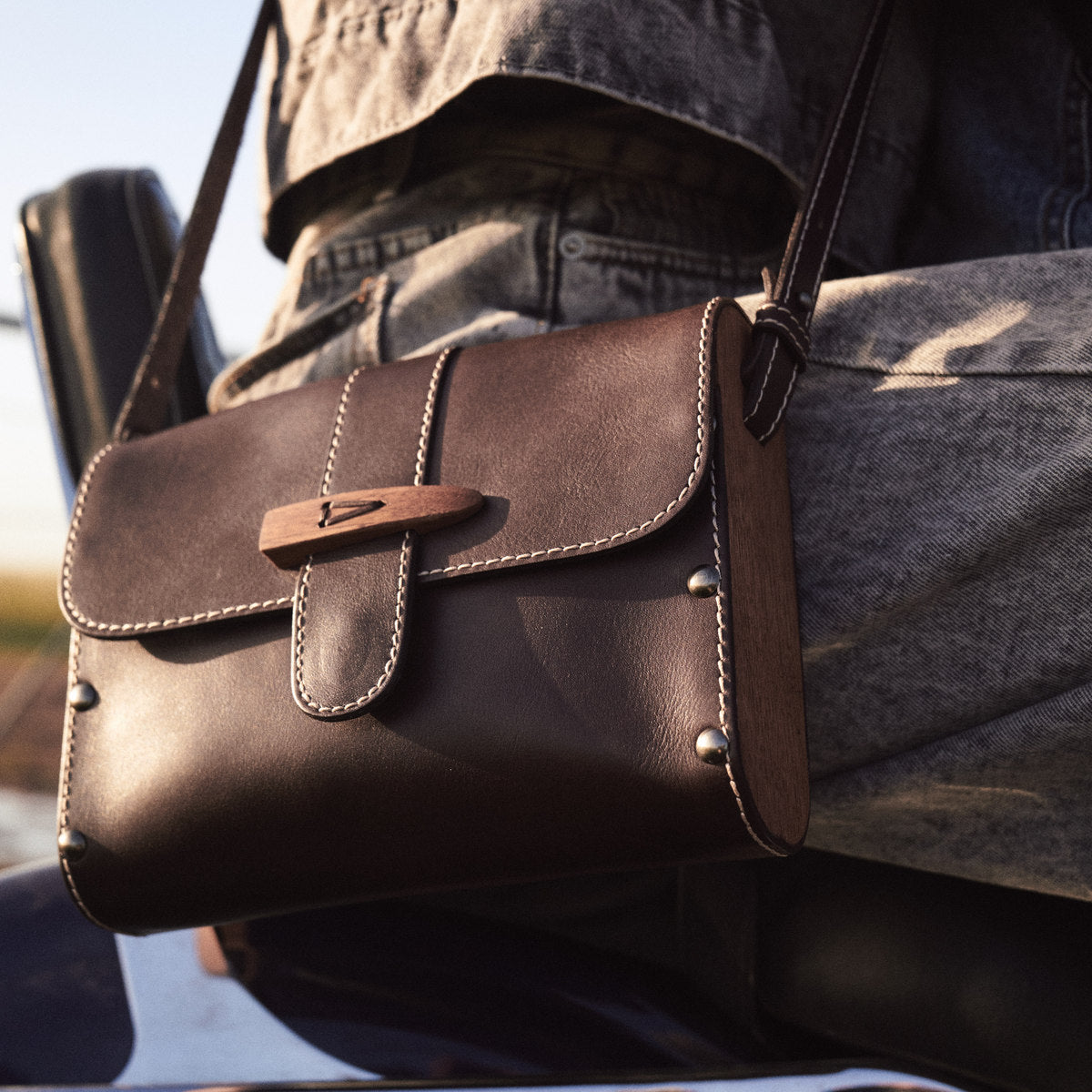 Close-up of the Sally satchel in brown hanging from a motorbike seat, wooden toggle and studs